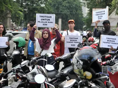 Koalisi Pejalan Kaki membawa poster saat menggelar aksi Tamasya Trotoar Kita di lokasi parkir liar sepanjang jalur pedestrian Gelora Bung Karno (GBK), Jakarta, Minggu (9/12). (Merdeka.com/Iqbal S. Nugroho)