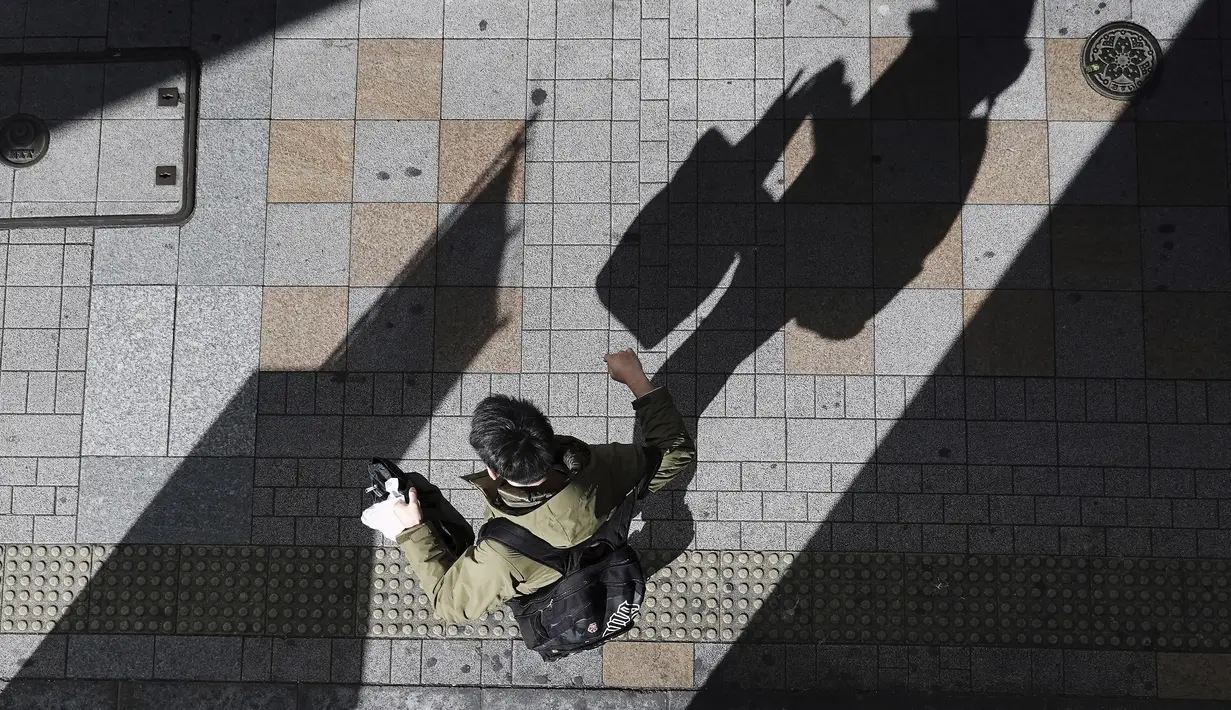 Seorang pria yang mengenakan masker pelindung untuk membantu mengekang penyebaran Virus Corona berjalan di sepanjang jalan di Tokyo (19/1/2021). Ibukota Jepang itu mengonfirmasi lebih dari 1.200 kasus Virus Corona baru pada 19 Januari 2021. (AP Photo/Eugene Hoshiko)