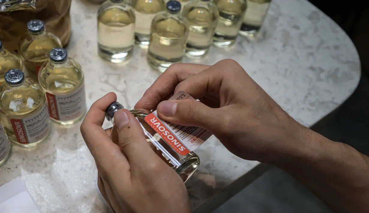 Seorang karyawan meletakkan label pada botol minuman Sinosovr, minuman yang terinspirasi oleh vaksin virus corona Covid-19, di sebuah bar koktail di George Town di pulau Penang, Malaysia (8/9/2021). (AFP/Mohd Rasfan)