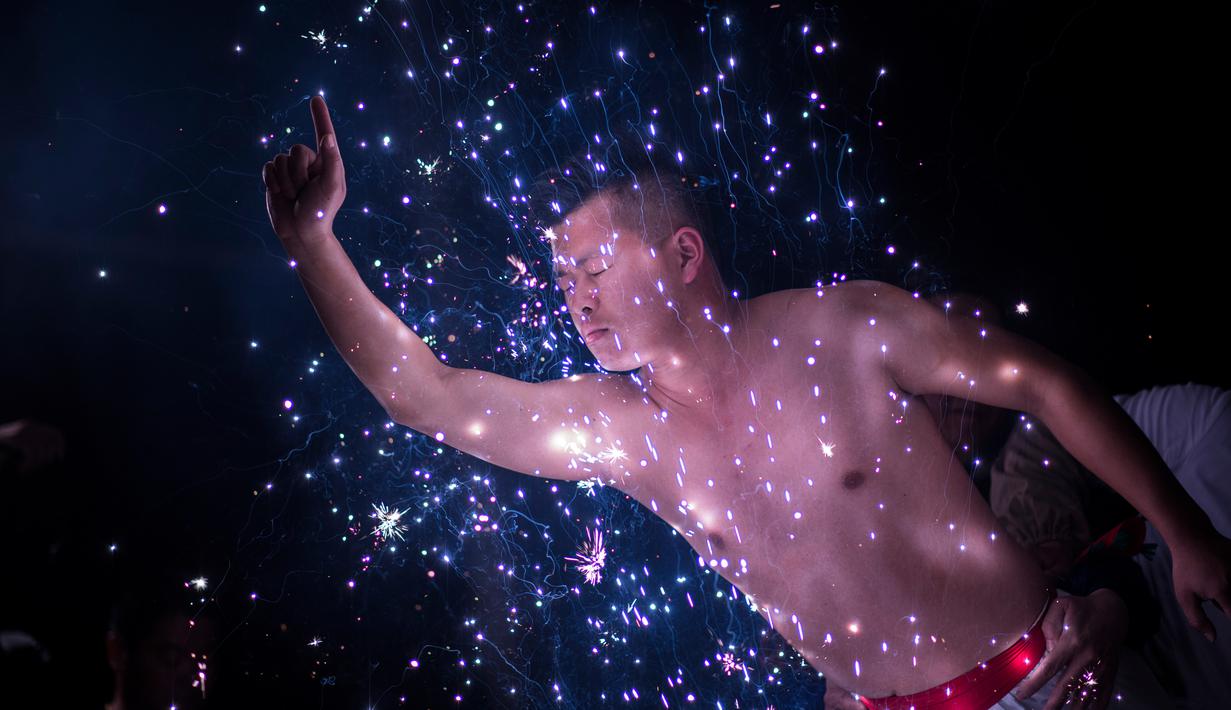 Seorang pria bermandikan percikan kembang api saat mengikuti ritual eating flowers di provinsi Fujians, China (16/2). Ritual unik ini digelar untuk mengusir roh-roh jahat. (AFP/Johannes Eisele)