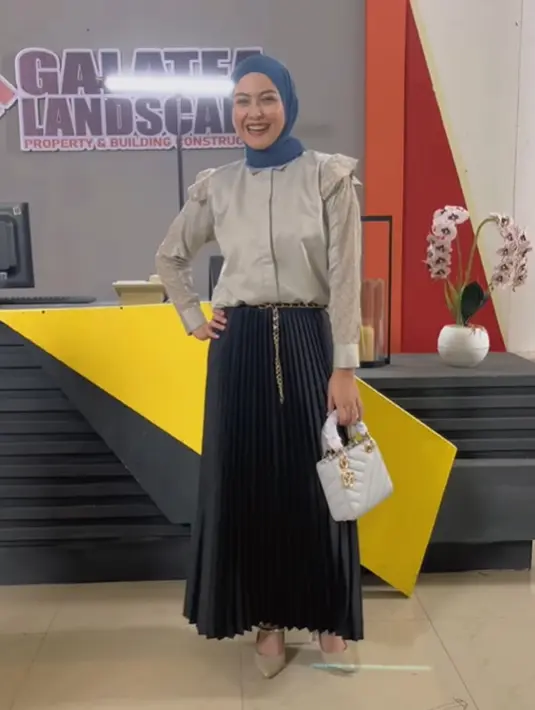 Di sini Revalina tampil anggun dengan kemeja silk yang dipadukan dengan rok lipit. [Foto: Instagram/vatemat]