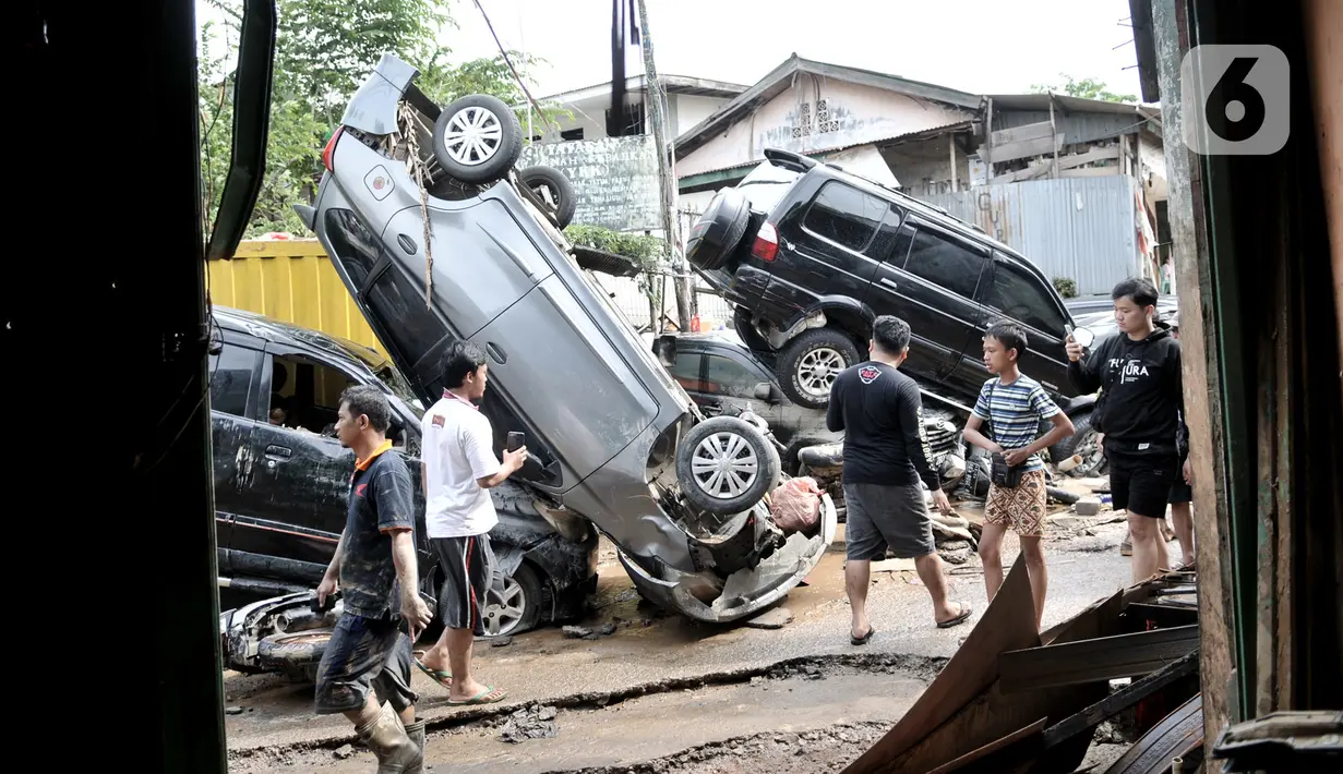 Warga melintasi sejumlah mobil yang terbalik akibat terjangan banjir di Perumahan Pondok Gede Permai, Jatiasih, Kota Bekasi, Jawa Barat, Kamis (2/1/2020). Derasnya terjangan banjir menyebabkan puluhan mobil terbalik dan belasan sepeda motor ringsek akibat terbawa arus. (merdeka.com/Iqbal Nugroho)