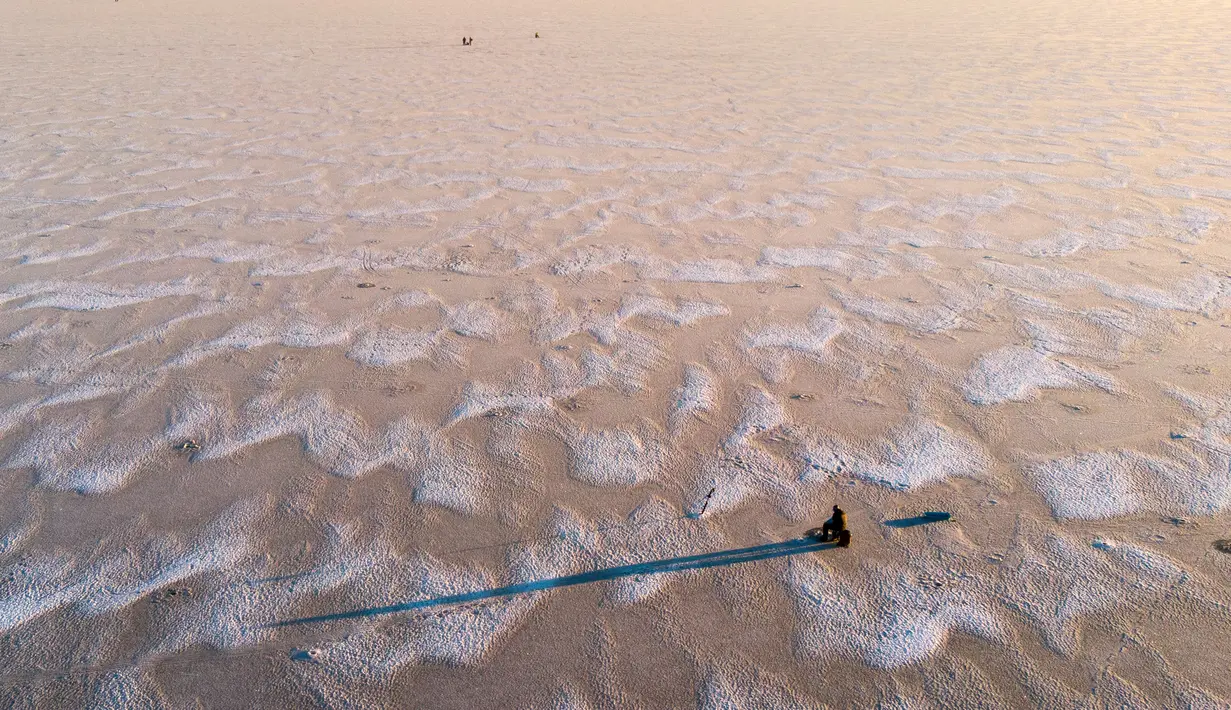 Seorang pria sedang memancing di tengah Laut Bothnia yang membeku di dekat Vaasa, Finlandia, 28 Desember 2018. Sebelum memancing, mereka membuat lubang menggunakan bor untuk memberikan umpannya kepada ikan buruan. (OLIVIER MORIN / AFP)