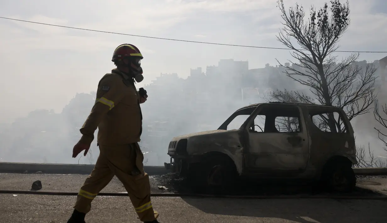 Seorang petugas pemadam kebakaran berjalan di samping mobil yang terbakar selama kebakaran hutan di pinggiran Voula, di selatan Athena, Yunani, Sabtu, 4 Juni 2022. Awan asap tebal imbas dari kebakaran hutan itu pun menganggu aktivitas di wilayah pinggiran selatan Yunani. (AP Photo/Yorgos Karahalis)