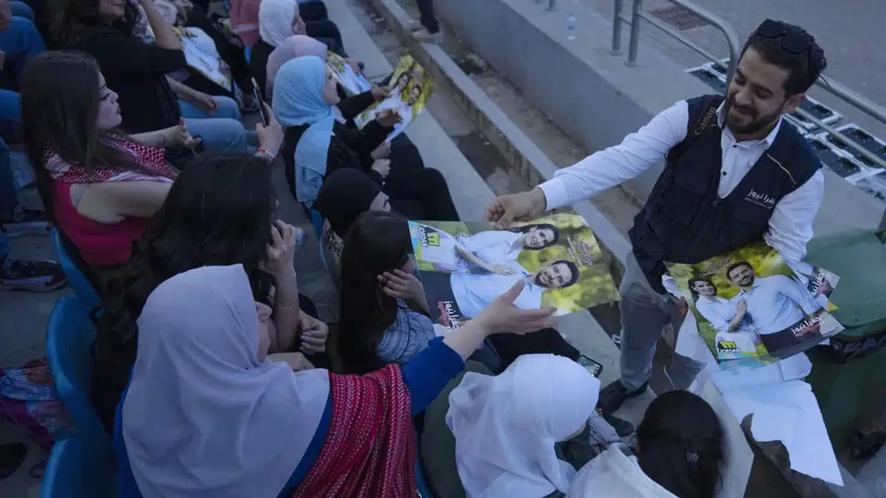 Seorang pria membagikan poster Putra Mahkota Yordania Hussein dan tunangannya, Rajwa Alseif, saat konser di stadion olahraga di Amman, Yordania, Senin, (29/5/2023). (Foto: AP/Nasser Nasser)