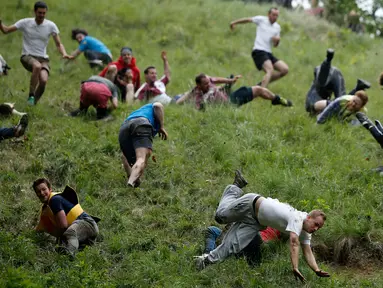 Sejumlah peserta saling berjatuhan saat mengejar gulungan keju yang diturunkan dari atas bukit Cooper Hill dalam kompetisi tahunan, Cheese Rolling di Brockworth, Gloucestershire, Inggris, 30 Mei 2016. (Adrian DENNIS/AFP)