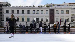 Orang-orang yang memakai masker mendengarkan pelatih ice skating di arena depan Balai Kota Athena, Kamis (23/12/2021). Yunani membatalkan konser Natal dan acara lainnya sebagai bagian dari pembatasan baru yang mencakup mandat penggunaan masker di luar ruangan. (AP Photo/Thanassis Stavrakis)