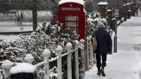 Seorang pria berjalan melewati box telefon yang tertutup salju tebal di Marlow, Inggris, Senin (11/12/2017). (AP)