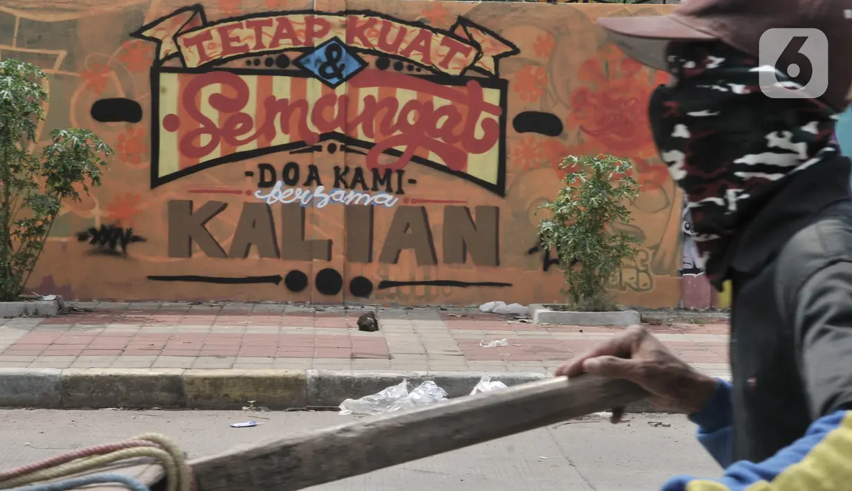 Pemulung melintas di depan mural dukungan untuk tim medis Covid-19 di kawasan Sunter, Jakarta, Rabu (27/5/2020). Mural tersebut sebagai bentuk dukungan untuk tim medis penanganan Covid-19 sekaligus mengingatkan masyarakat agar taat mengikuti aturan PSBB. (merdeka.com/Iqbal S. Nugroho)