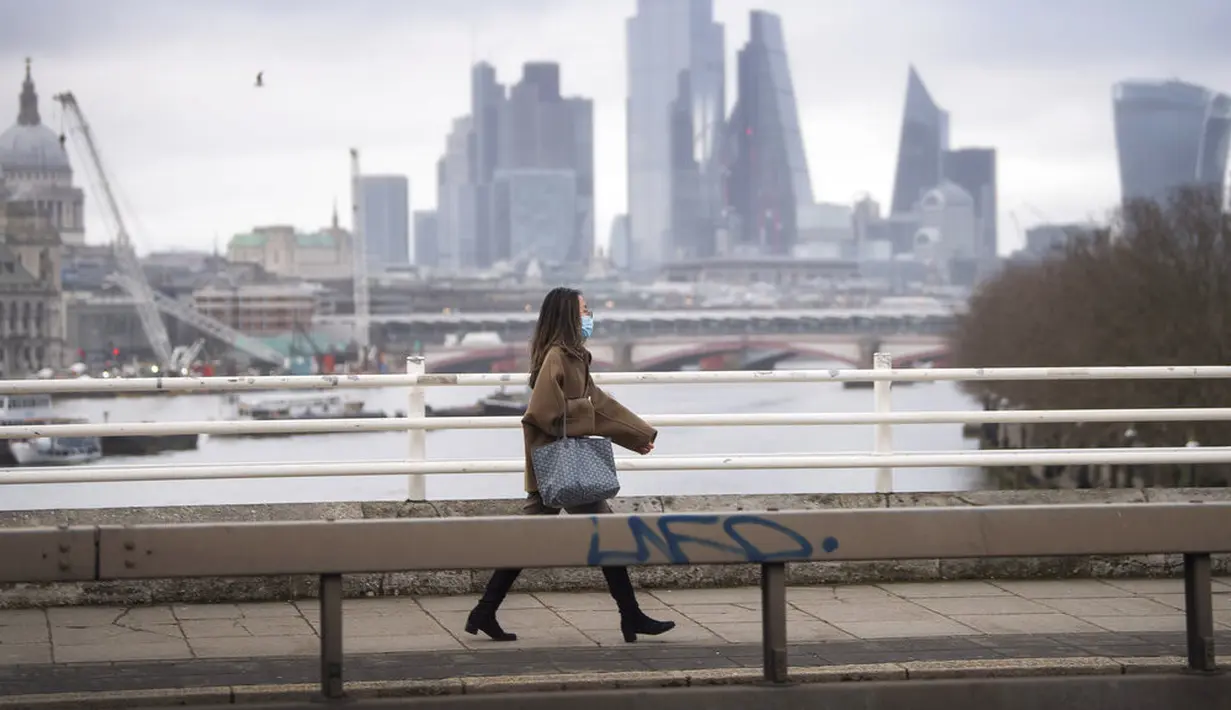 Seorang wanita yang mengenakan masker berjalan di atas Waterloo Bridge yang kosong, London, Inggris, 12 Januari 2021. Inggris sedang menerapkan lockdown nasional ketiga untuk mengekang penyebaran virus corona COVID-19. (Victoria Jones/PA via AP)