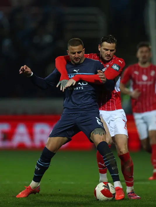 Bek Manchester City Kyle Walker (kiri) bersaing dengan gelandang tim divisi 4 Swindon Town, Ben Gladwin (kanan) dalam duel putaran ketiga Piala FA 2021/22 di County Ground, Sabtu (8/1/2022) dini hari WIB. Manchester City menang telak 4-1 saat menghadapi Swindon Town. (Adrian DENNIS / AFP)