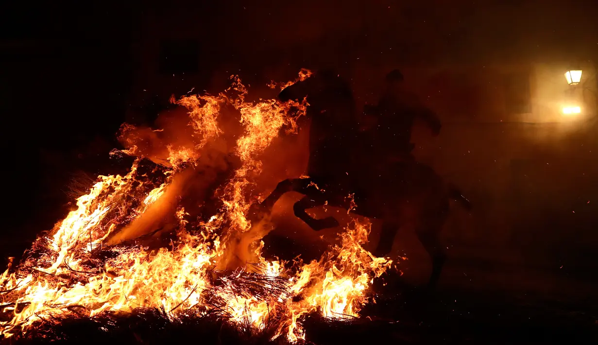 Seorang pria menunggangi kuda melewati api unggun saat festival Luminarias di San Bartolome de Pinares, Spanyol, Jumat (16/1/2020). Festival tersebut menjadi daya tarik wisatawan domestik dan mancanegara untuk datang ke Desa San Bartolomeo de Pinares. (AP Photo/Manu Fernandez)