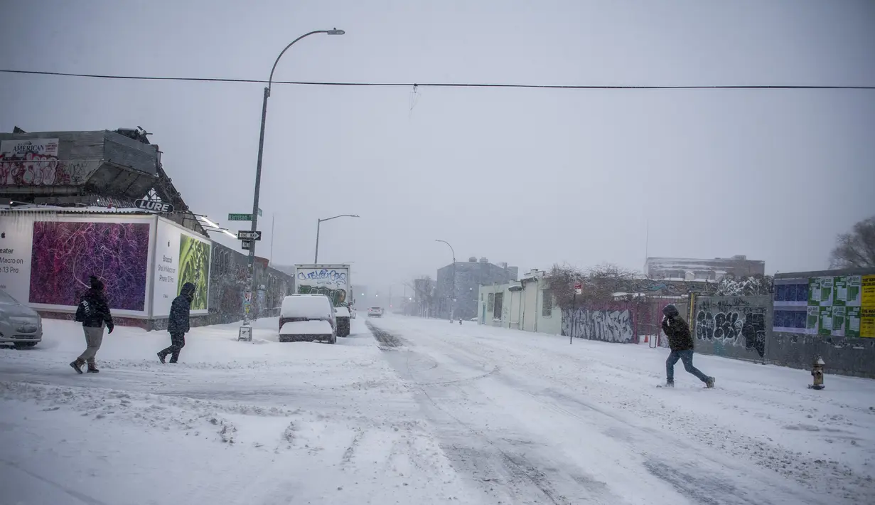 Orang-orang menyeberang jalan selama badai salju di bagian Bushwick di wilayah Brooklyn di New York, Sabtu (29/1/2022). Orang-orang dari New York City hingga Maine terbangun karena salju tebal dan angin kencang saat badai Nor'easter yang kuat melanda. (AP Photo/Brittainy Newman)