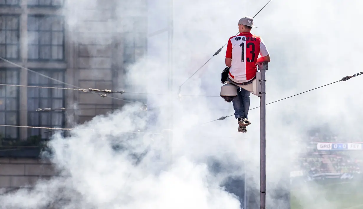 Seorang suporter Feyenoord duduk di tiang kamera merayakan gelar juara Eredivisie Belanda di Coolsingel, Rotterdam (15/5). (AFP Photo/ANP/Marco de Swart/Netherlands Out)