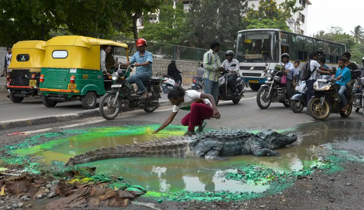 Sejumlah pengguna jalan memperhatikan aksi Seniman Baadal Nanjundaswamy saat menyelesaikan boneka buaya di atas jalan berlubang di Sultanpalya, Bangalore, India, Kamis (18/6/2015). (AFP PHOTO/ Manjunath KIRAN)