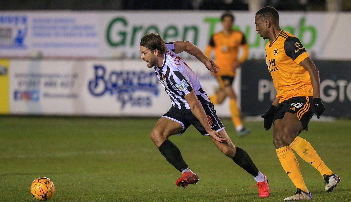 Gelandang Chorley, Harry Cardwell (kiri) menguasai bola dibayangi bek Wolverhampton Wanderers, Willy Boly dalam laga babak keempat Piala FA 2020/21 di Victory Park Stadium, Jumat (22/1/2021). Chorley kalah 0-1 dari Wolverhampton. (AFP/Lindsey Parnaby)