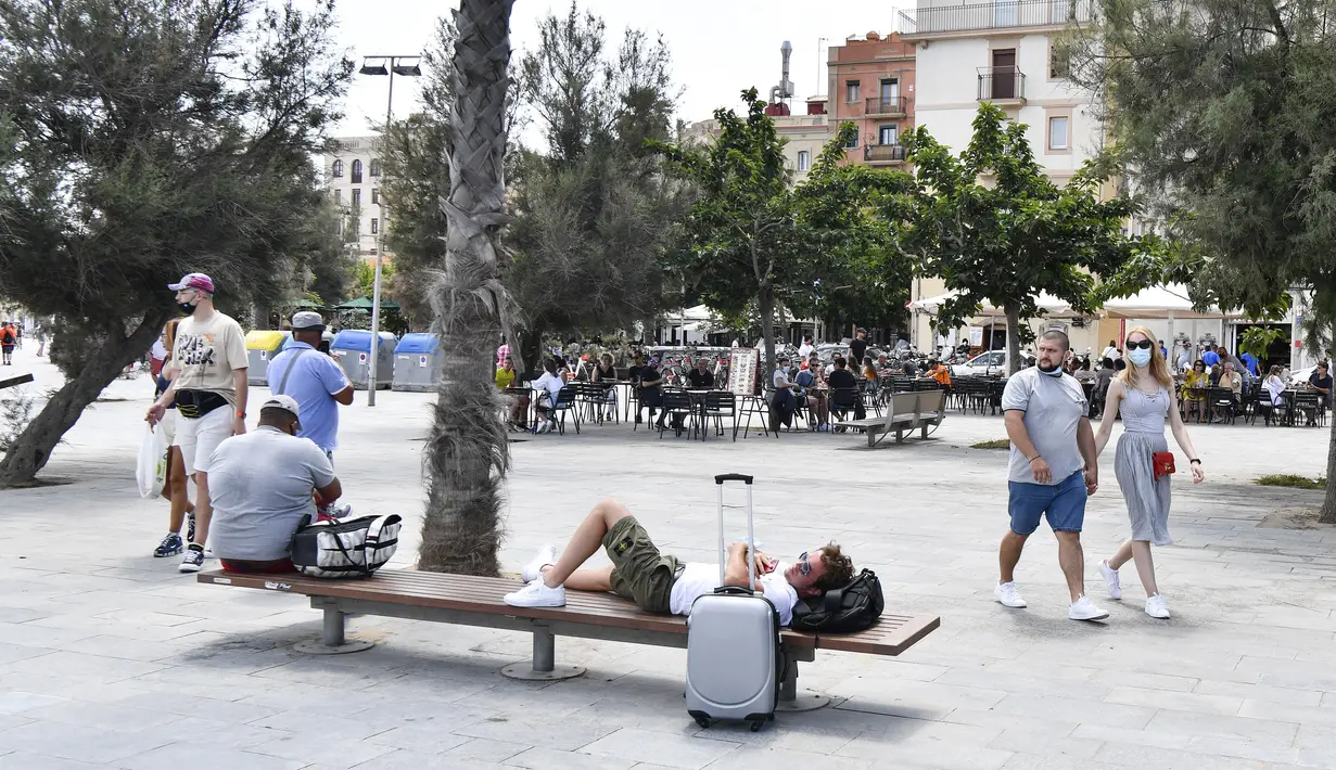 Orang-orang berjalan di kawasan pejalan kaki di Pantai Barceloneta, Barcelona, Minggu (6/6/2021). Spanyol akan mengizinkan semua pelancong yang divaksinasi untuk mengunjungi negaranya mulai 7 Juni, dengan tujuan kembali menghidupkan industri perjalanan yang dilanda pandemi Covid-19 (Pau BARRENA/AFP)
