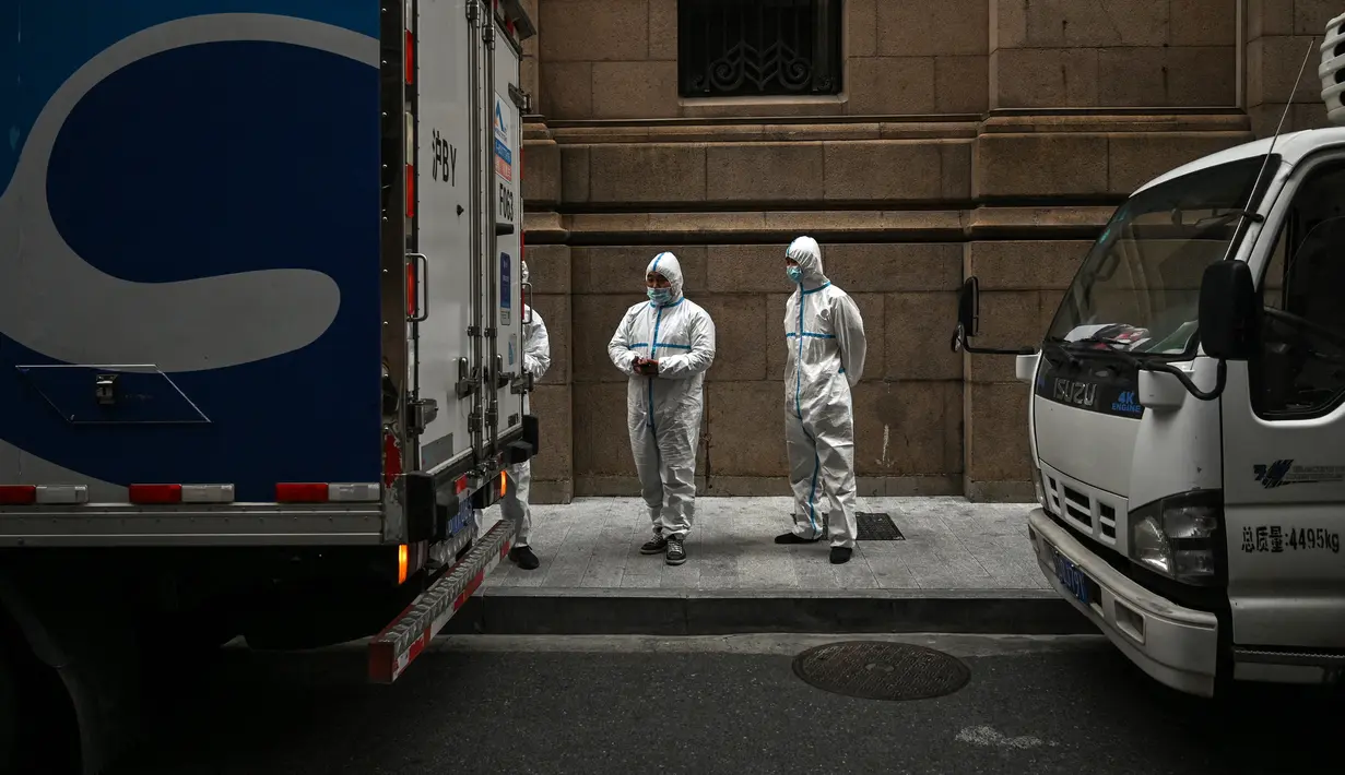 Pekerja yang mengenakan alat pelindung diri berdiri di sebelah akses hotel di Bund, Puxi, Shanghai, China, 31 Maret 2022. Daerah Puxi akan lockdown mulai 1 April 2022. (Hector RETAMAL/AFP)