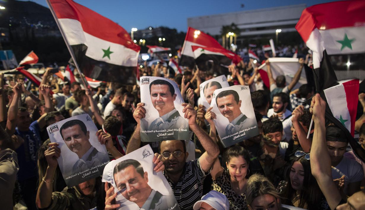 Pendukung mengibarkan bendera nasional dan foto Presiden Suriah Bashar Assad saat mereka merayakan kemenangannya di Omayyad Square, di Damaskus, Kamis (27/5/2021). Bashar al-Assad terpilih kembali untuk masa jabatan keempat sebagai presiden Suriah yang dilanda perang. (AP Photo/Hassan Ammar)