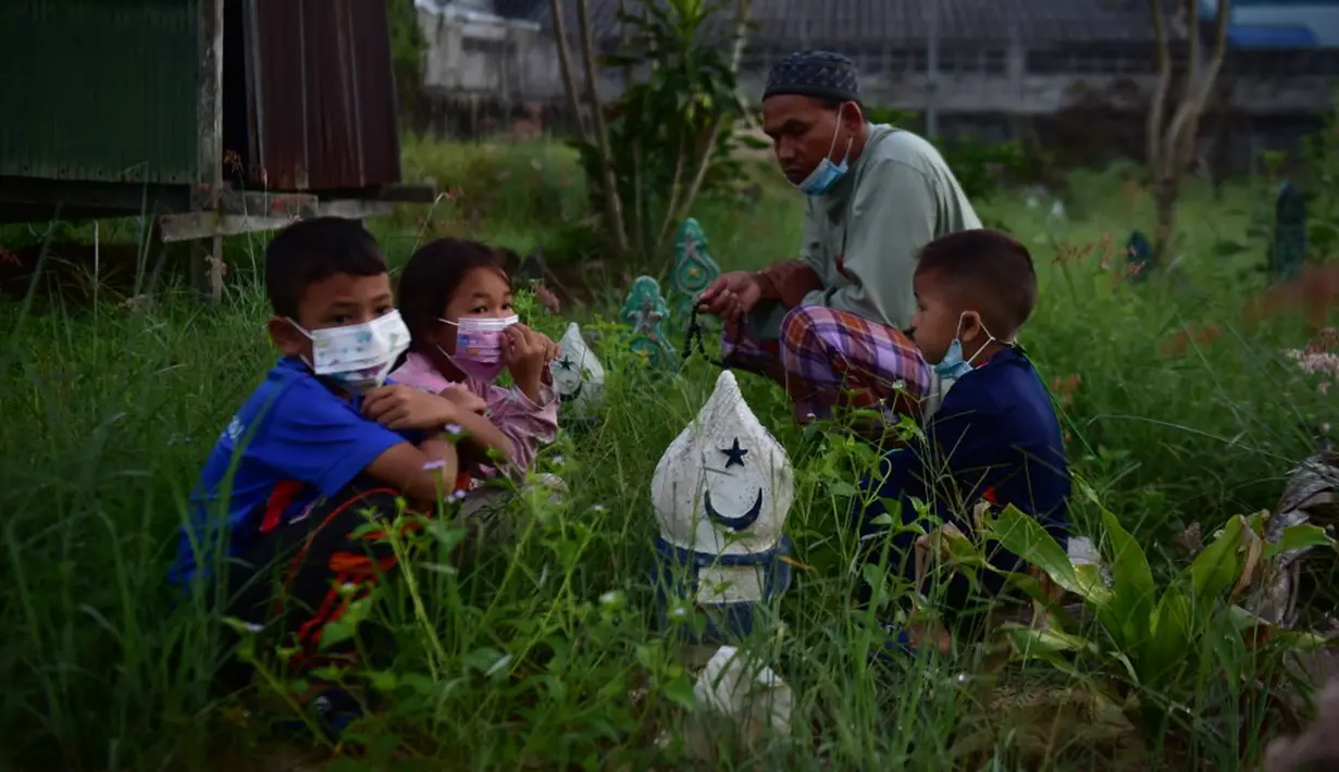 Orang-orang berdoa di sebelah makam kerabat saat perayaan Hari Raya Idul Adha di sebuah pemakaman di Provinsi Narathiwat, Thailand, Rabu (21/7/2021). Setiap Idul Adha atau hari besar Islam lainnya, sebagian warga banyak mendatangi kuburan untuk mendoakan keluarganya. (Madaree TOHLALA/AFP)