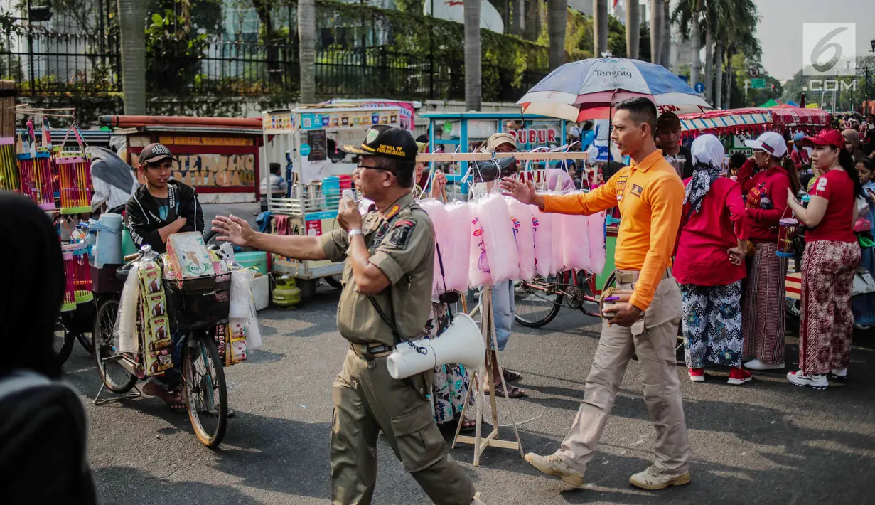 Petugas Satpol PP melakukan sosialisasi saat menertibkan PKL di kawasan car free day (CFD), Bundaran HI, Jakarta, Minggu (4/8/2019). Penertiban dilakukan karena keberadaan PKL membuat tidak nyaman pengunjung CFD yang ingin berolahraga, berorasi, atau sekadar jalan-jalan. (Liputan6.com/Faizal Fanani)