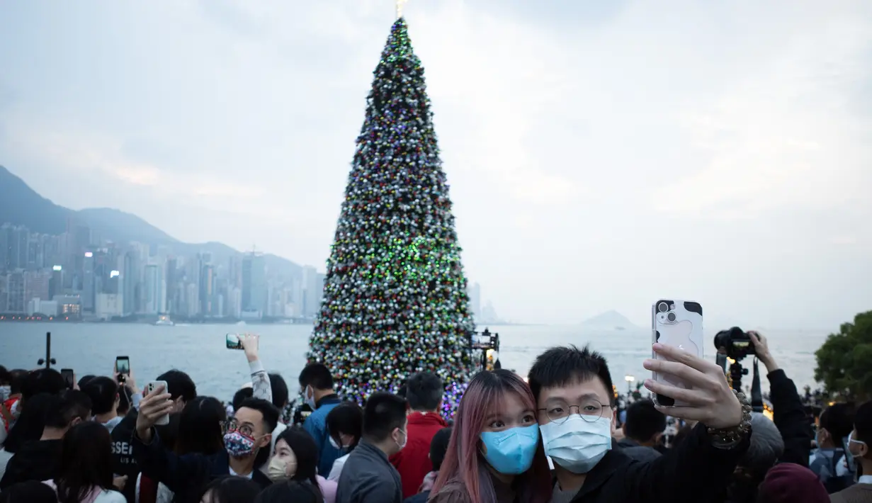 Sepasang kekasih berpose di depan pohon Natal raksasa saat Natal di distrik budaya West Kowloon di Hong Kong (25/12/2021). Pohon Natal raksasa ini memiliki ukuran setinggi 20 meter. (AFP/Bertha Wang)