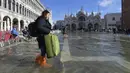 Seorang wanita berjalan di St. Mark's Square yang terendam banjir di Venesia, Italia, Jumat (5/11/2021). Setelah Venesia mengalami banjir terparah kedua dalam sejarahnya pada November 2019, kota itu dibanjiri empat kali pasang luar biasa dalam waktu enam minggu. (AP Photo/Luigi Costantini)