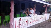 Agustinus Sasuwu memainkan salah satu alat musik bambu di depan rumahnya. (Liputan6.com/Yoseph Ikanubun)