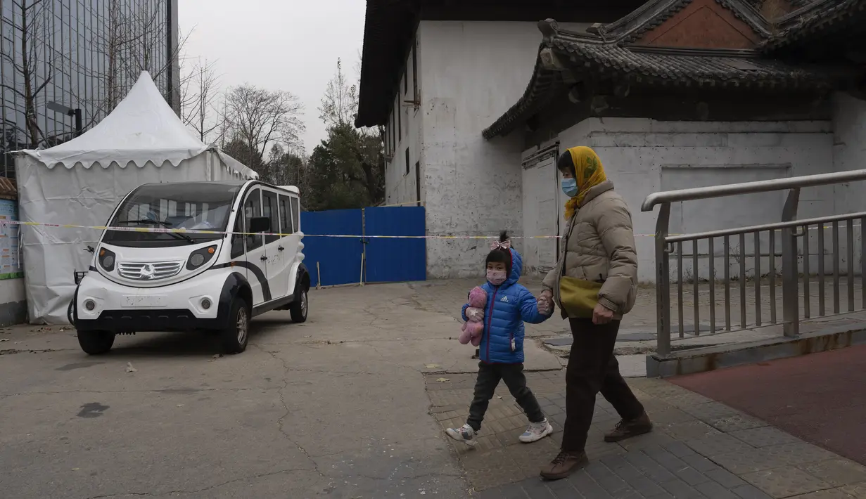 Seorang perempuan dan anak-anak yang memakai masker berjalan di dekat area tertutup di Beijing, China, Jumat (2/12/2022). Lebih banyak kota melonggarkan pembatasan, memungkinkan pusat perbelanjaan, supermarket, dan bisnis lainnya dibuka kembali menyusul protes akhir pekan lalu di Shanghai dan daerah lain di mana beberapa orang menyerukan Presiden Xi Jinping untuk mengundurkan diri. (AP Photo/Ng Han Guan)