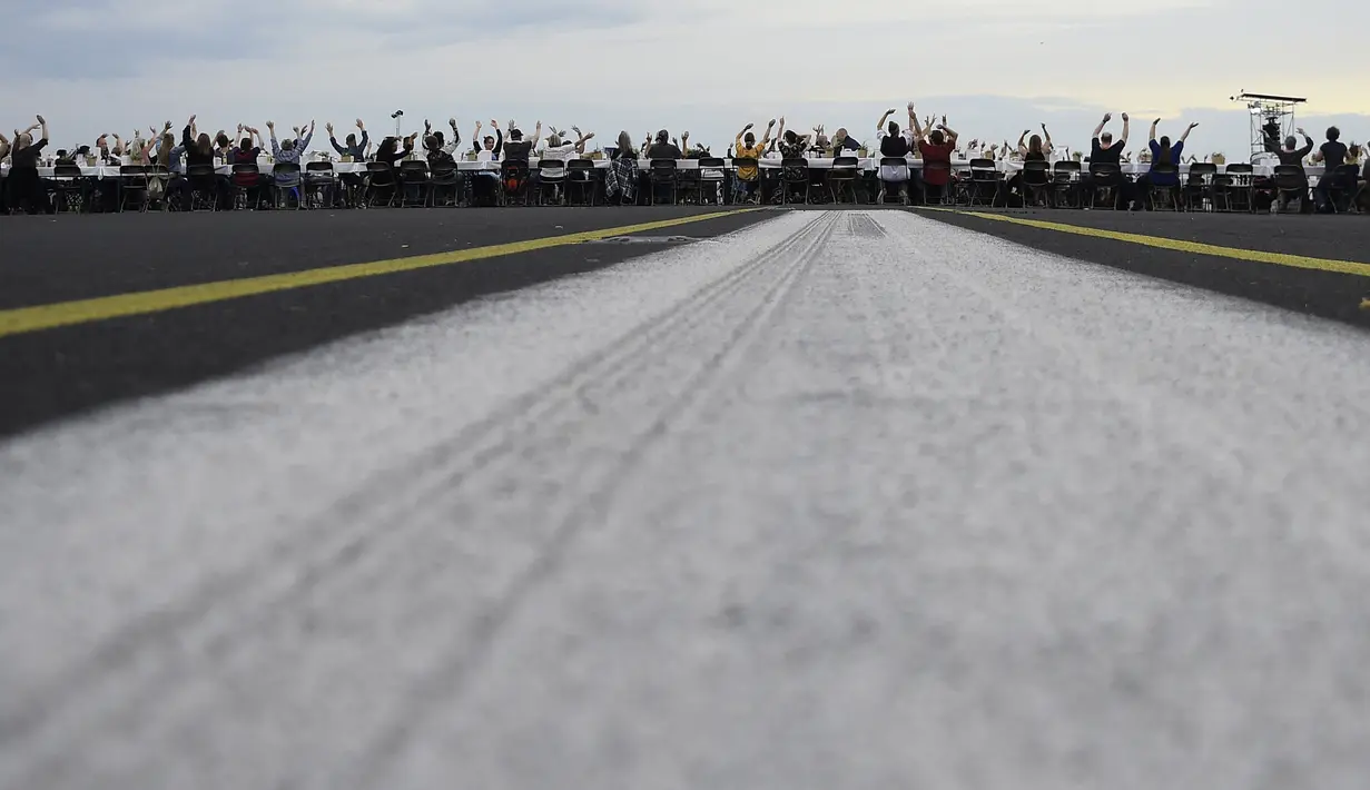 Para tamu melambai ke arah helikopter yang terbang di atas meja mereka saat acara “Berlin Freedom Dinner” di landasan pacu bekas bandara Tegel, Berlin pada 7 Agustus 2021. Acara itu untuk mengirim sinyal 'Berlin kembali!' setelah berbulan-bulan menghadapi pandemi COVID-19. (Tobias SCHWARZ/AFP)