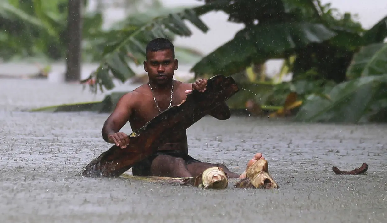 Seorang lelaki menggunakan kayu sebagai perahu saat banjir melanda Sri Lanka, Minggu (28/5). Saat ini tercatat sudah ada 122 orang yang kehilangan nyawanya akibat bencana yang dipicu oleh hujan lebat di Sri Lanka. (AP Photo)