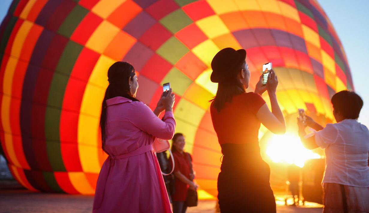 Wisatawan mengambil gambar saat balon udara disiapkan untuk menikmati pemandangan Kapadokia, Turki, Selasa (7/8). Kapadokia memiliki sejumlah keajaiban alam, khususnya Cerobong Peri (Fairy Chimney). (AP Photo/Emrah Gurel)