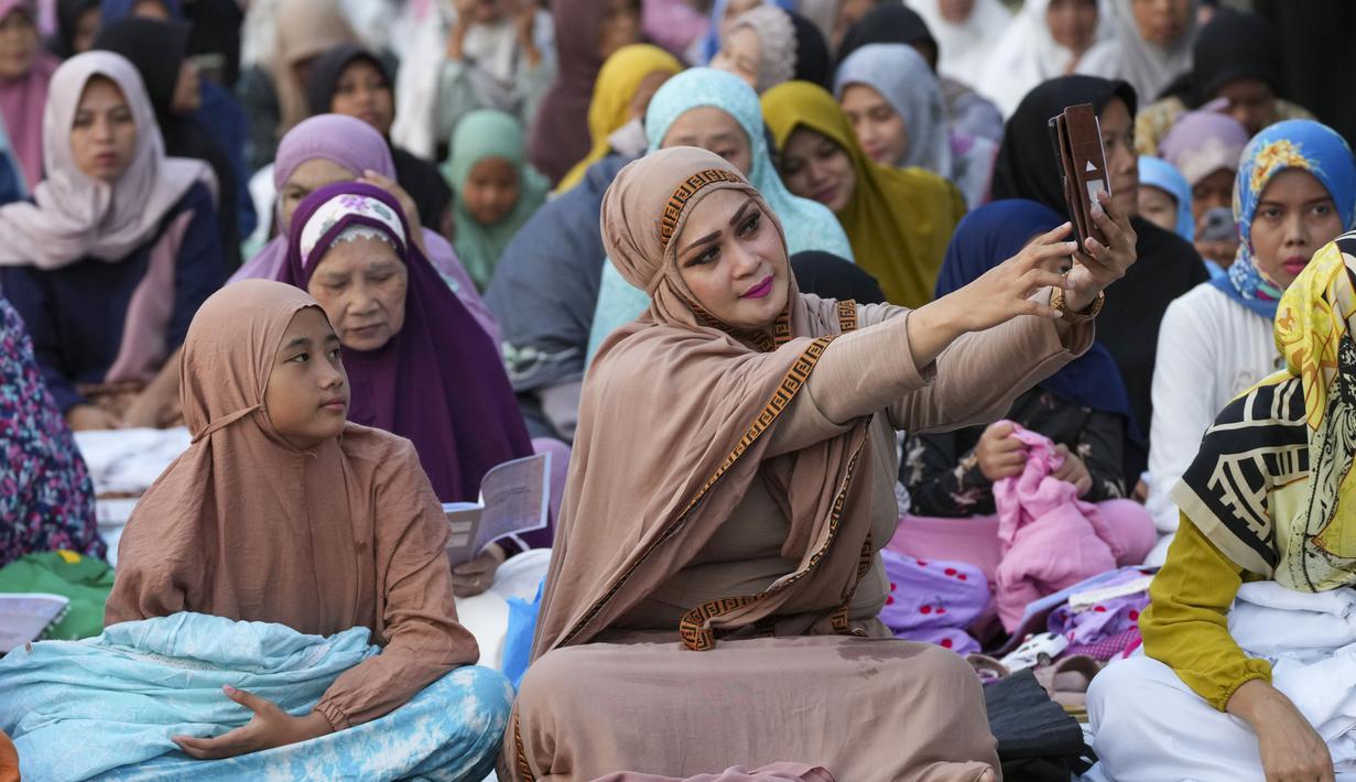 Seorang perempuan berswafoto sebelum sholat Idul Adha di sebuah jalan di Jakarta, Indonesia, Kamis, 29 Juni 2023. (AP Photo/Tatan Syuflana)