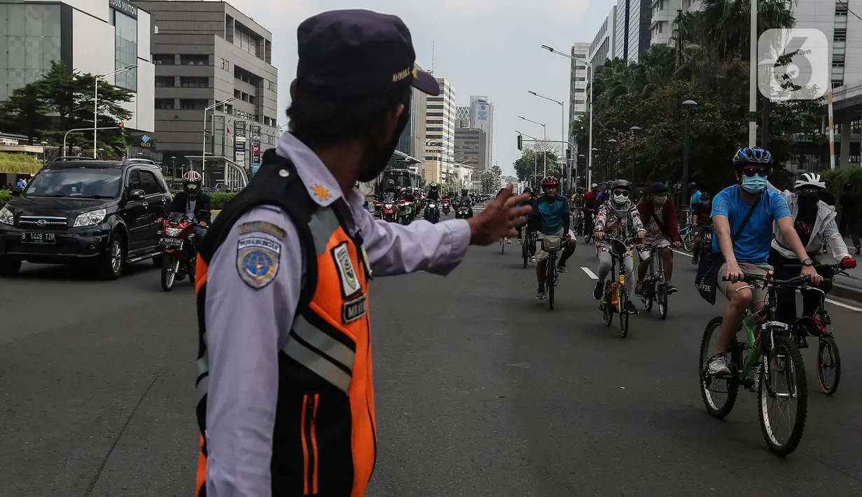 Petugas mengatur lalu lintas saat warga bersepeda di kawasan Thamrin, Jakarta Pusat, Minggu (15/11/2020). Di masa PSBB transisi Jakarta, warga tetap melakukan aktivitas olahraga, khususnya bersepeda yang kini banyak diminati bahkan menjadi tren. . (Liputan6.com/Johan Tallo)
