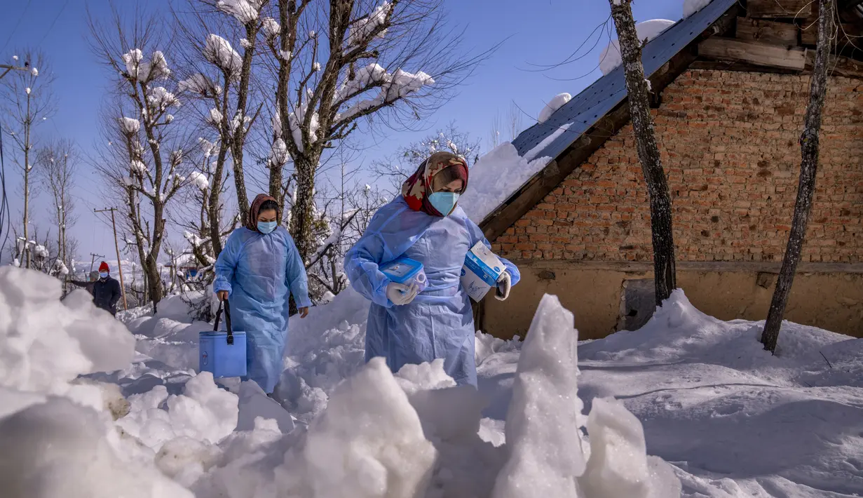 Fozia (kanan) dan Tasleema, petugas kesehatan Kashmir, membawa vaksin saat mereka berjalan di jalan yang tertutup salju selama upaya vaksinasi COVID-19 di Budgam, barat daya Srinagar, Kashmir yang dikuasai India, pada 11 Januari 2022. (AP Photo/Dar Yasin)