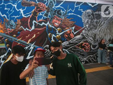Warga berswafoto dengan latar belakang mural kolaborasi di Terowongan Kendal, Kawasan TOD Dukuh Atas, Jakarta, Rabu (6/7/2022). Disney Indonesia berkolaborasi bersama Jakarta Experience Board (JXB) dan Kita Art Friends menghadirkan karya seni mural terinspirasi dari film Marvel Studios "Thor: Love and Thunder." (Liputan6.com/Faizal Fanani)