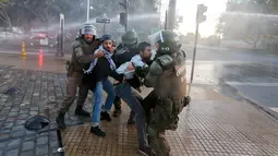 Polisi anti huru hara menarik dua orang pria saat terjadi unjuk rasa di luar kedutaan AS di Santiago, Chili (14/4). Serangan itu menyisakan puing-puing bangunan yang luluh lantak akibat rudal. (AP / Esteban Felix)