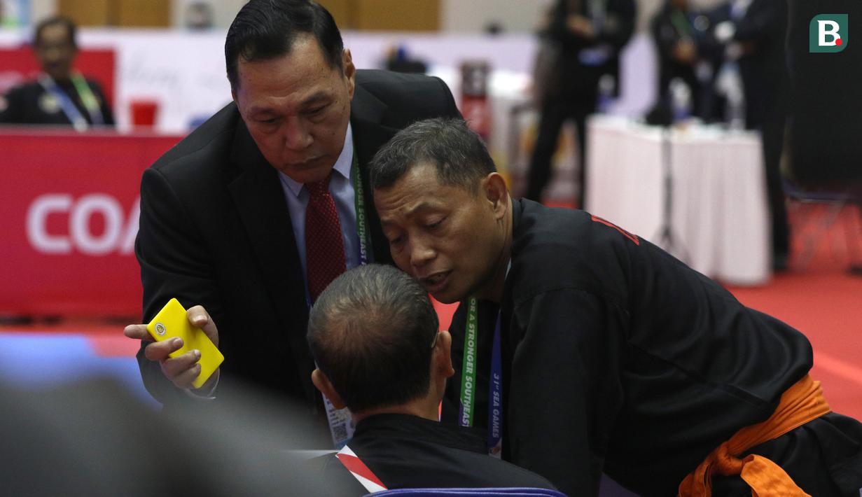 Ketua Harian PB Ikatan Pencak Silat Indonesia (IPSI) yang juga menjabat sebagai Ketua Eksekutif Persekutuan Pencak Silat Antarabangsa (Persilat), Benny Sumarsono (kiri) menghampiri dan terlibat argumentasi dengan pelatih pencak silat Indonesia, Bondan (tengah). (Bola.com/Ikhwan Yanuar)