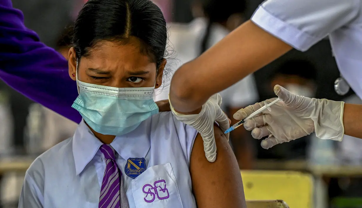 Seorang gadis sekolah bereaksi ketika seorang petugas kesehatan menyuntiknya dengan dosis vaksin Pfizer-BioNTech terhadap virus corona Covid-19 untuk kelompok usia 12-15 tahun di sebuah lembaga pendidikan di Kolombo, Sri Lanka (7/1/2022). (AFP/Ishara S. Kodikara)