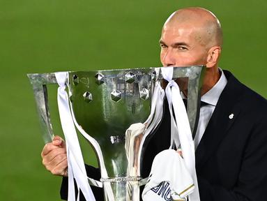 Pelatih Real Madrid, Zinedine Zidane, mengangkat trofi juara La Liga musim 2019/2020 usai timnya mengalahkan Villarreal pada laga lanjutan La liga di Estadio Alfredo Di Stefano, Jumat (17/7/2020) dini hari WIB. (AFP/Gabriel Bouys)