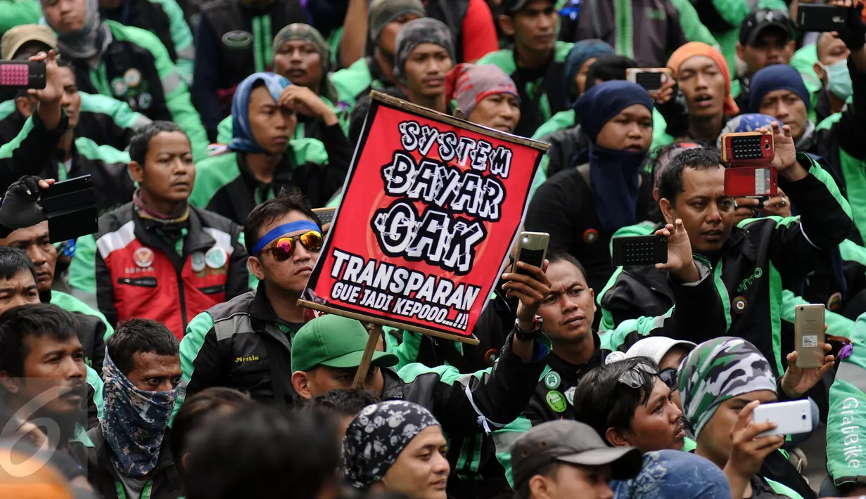 Pengemudi ojek on-line GrabBike mengangkat tulisan tuntutan saat unjuk rasa di belakang kantor Grab di kawasan Kuningan, Jakarta, Kamis (5/1). Mereka menuntut pihak perusahaan menaikkan tarif argo per kilometernya. (Liputan6.com/Helmi Fithriansyah)