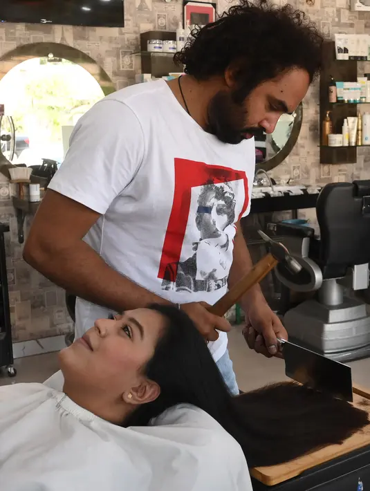 Dalam gambar pada 8 April 2021, tukang cukur Pakistan Ali Abbas menggunakan palu dan pisau daging untuk memotong rambut pelanggan di tokonya di Lahore. Berharap membuktikan kemampuannya dalam persaingan, Ali Abbas mengandalkan berbagai alat yang tidak biasa untuk melatih keahliannya. (Arif ALI/AFP)