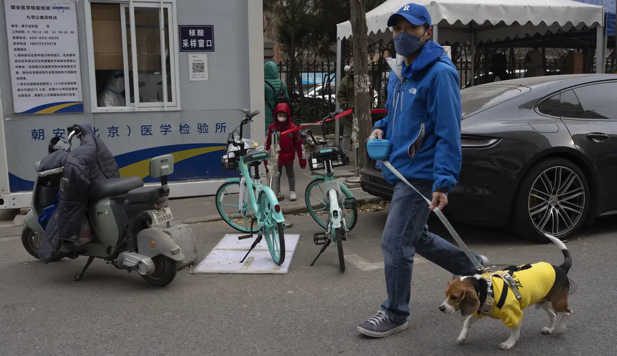 Seorang pria berjalan dengan anjingnya melewati stasiun pengujian COVID di Beijing, China, Jumat (2/12/2022). Lebih banyak kota melonggarkan pembatasan, memungkinkan pusat perbelanjaan, supermarket, dan bisnis lainnya dibuka kembali menyusul protes akhir pekan lalu di Shanghai dan daerah lain di mana beberapa orang menyerukan Presiden Xi Jinping untuk mengundurkan diri. (AP Photo/Ng Han Guan)