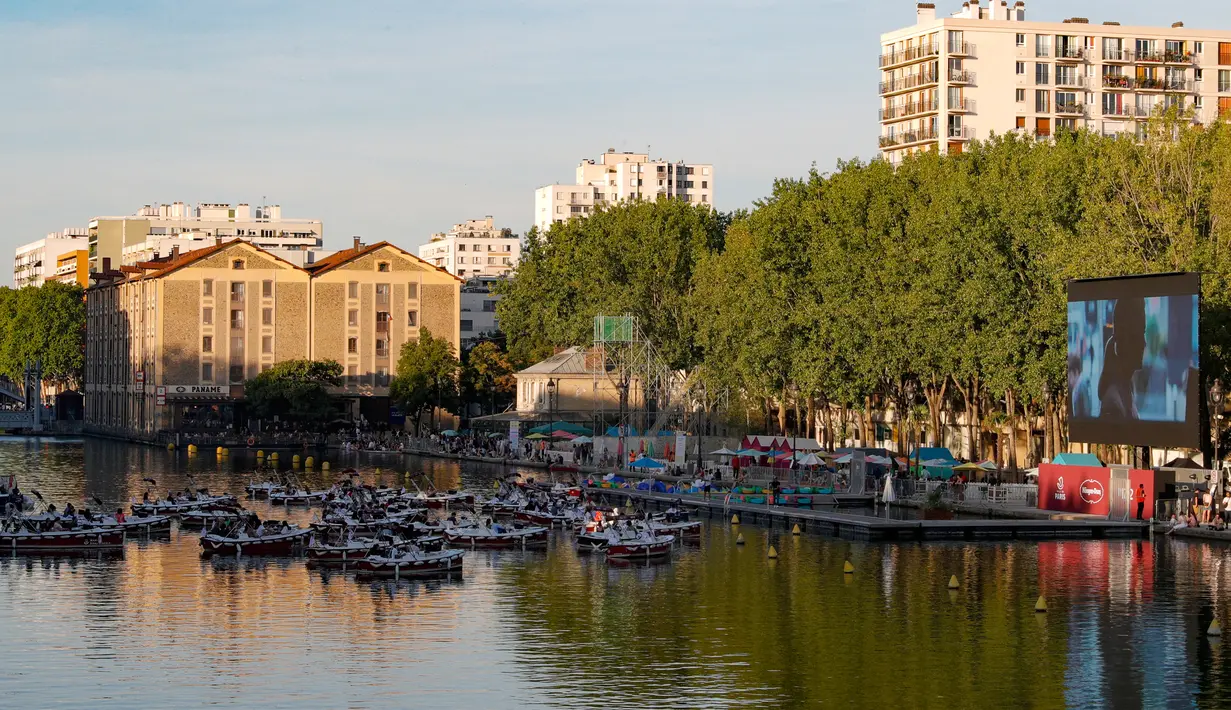 Orang-orang menghadiri pemutaran film "Le grand bain" pada hari pertama acara musim panas "Paris-Plages" di La villette bassin, Paris, 18 Juli 2020. Paris menghadirkan sebuah terobosan baru dengan bioskop terapung lengkap dengan perahu yang tetap menjaga jarak sosial. (GEOFFROY VAN DER HASSELT/AFP)