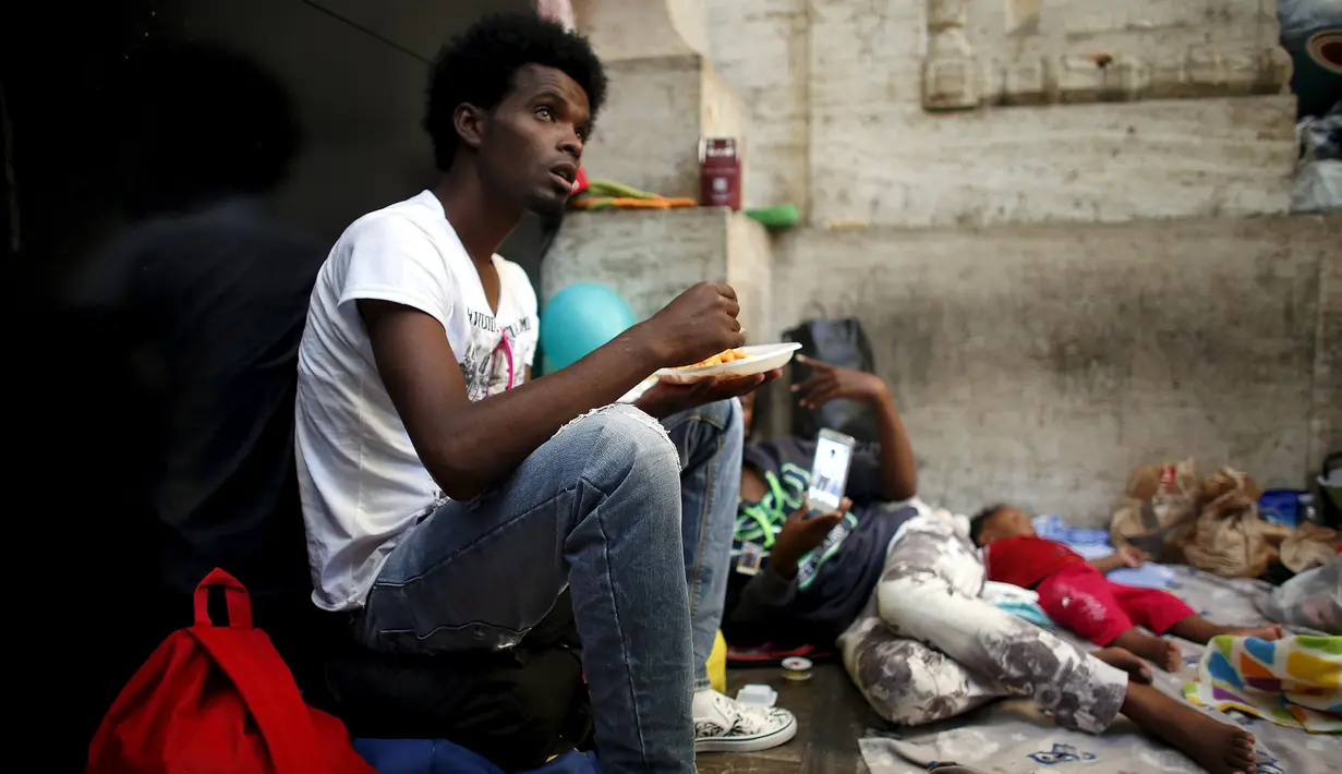 Seorang imigran tampak sedang makan di dekat stasiun kereta api Milan, 11 Juni 2015. Ratusan imigran yang baru diselamatkan beberapa pekan lalu dari laut oleh Italia ini hidup terlantar di sepanjang jalan. (REUTERS/Stefano Rellandini)