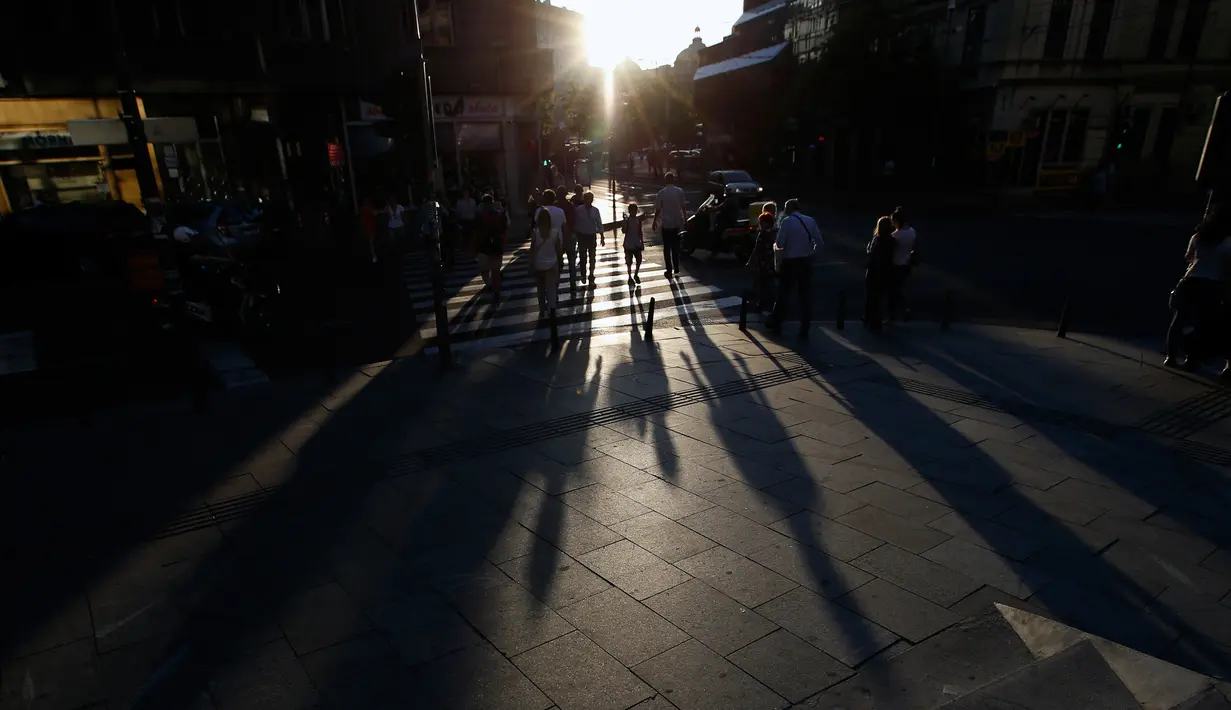 Orang-orang berjalan selama matahari terbenam di pusat kota Belgrade, Serbia, (29/5). Para ahli meteorologi meramalkan cuaca cerah di Serbia akan melanda beberapa hari mendatang. (AP Photo / Darko Vojinovic)
