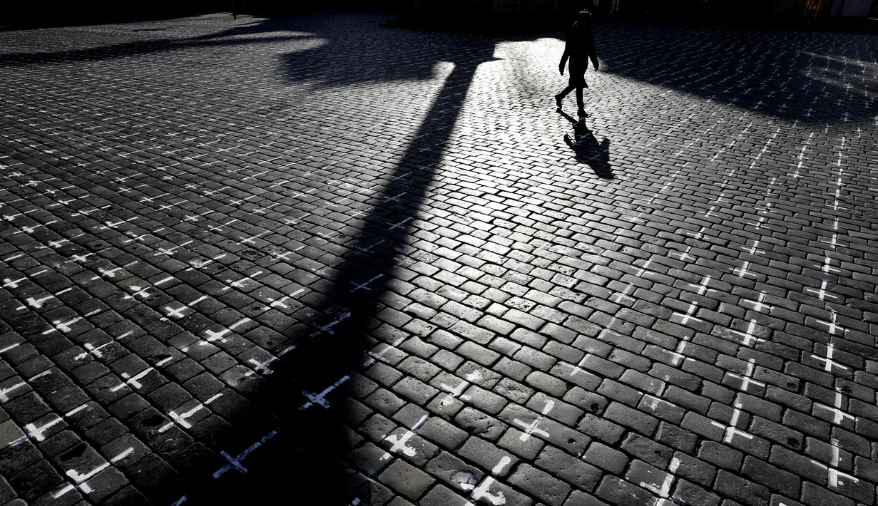 Seorang perempuan melintasi Alun-alun Kota Tua di Praha di mana ribuan salib dilukis untuk menandai satu tahun sejak kematian pertama akibat Covid-19 di Republik Ceko, Senin (22/3/2021). Sekelompok aktivis melukis salib untuk mengkritik tanggapan pemerintah terhadap pandemi. (AP/Petr David Josek)