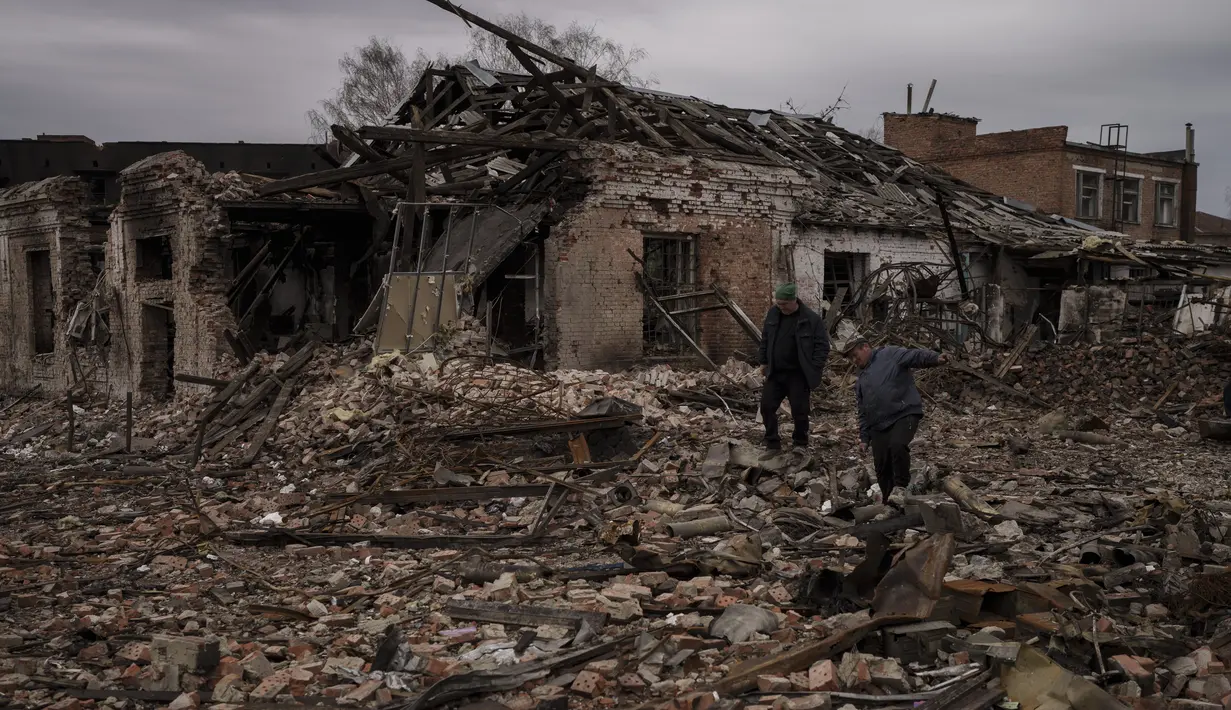 Warga berjalan di atas puing-puing bangunan yang hancur di kota Trostsyanets, Ukraina, Senin, 28 Maret 2022. Trostsyanets baru-baru ini direbut kembali oleh pasukan Ukraina setelah dikuasai oleh Rusia sejak awal perang. (AP Photo/Felipe Dana)