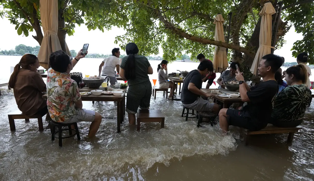 Pelanggan menyantap makanan di tengah banjir yang merendam Chaopraya Antique Café di Sungai Chao Phraya, Bangkok, Thailand, Kamis (7/10/2021). Restoran yang dilanda banjir ini menjadi tempat makan tidak biasa di mana pengunjung menikmati santapan makanan dengan kaki terendam (AP Photo/Sakchai Lalit)