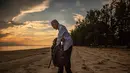 Tengku Mohamad Ali Mansor memeriksa botol kaca di sebuah pantai di desa Mangkuk, Malaysia timur pada 12 September 2020.  Upaya seorang lansia Malaysia untuk membersihkan pantai-pantai negara itu dari kaca-kaca yang terkelupas membuatnya mengumpulkan koleksi ribuan botol. (AFP/Mohd Rasfan)